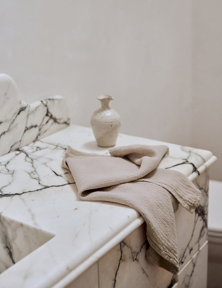 lifestyle shot of pure linen jacquard hand towel in natural colour with marble sink and decorative plants