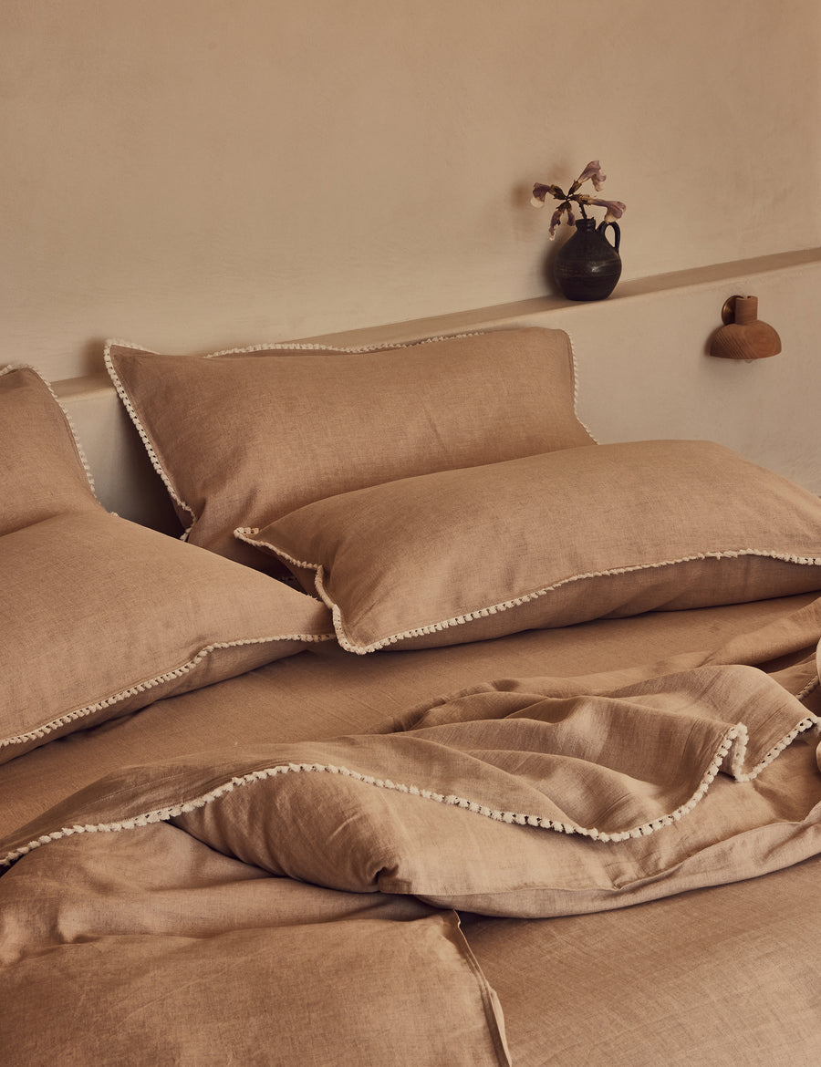 lifestyle shot of the linen quilt set in natural colour and finished in our contrast organic cotton tassel trim with rustic decor