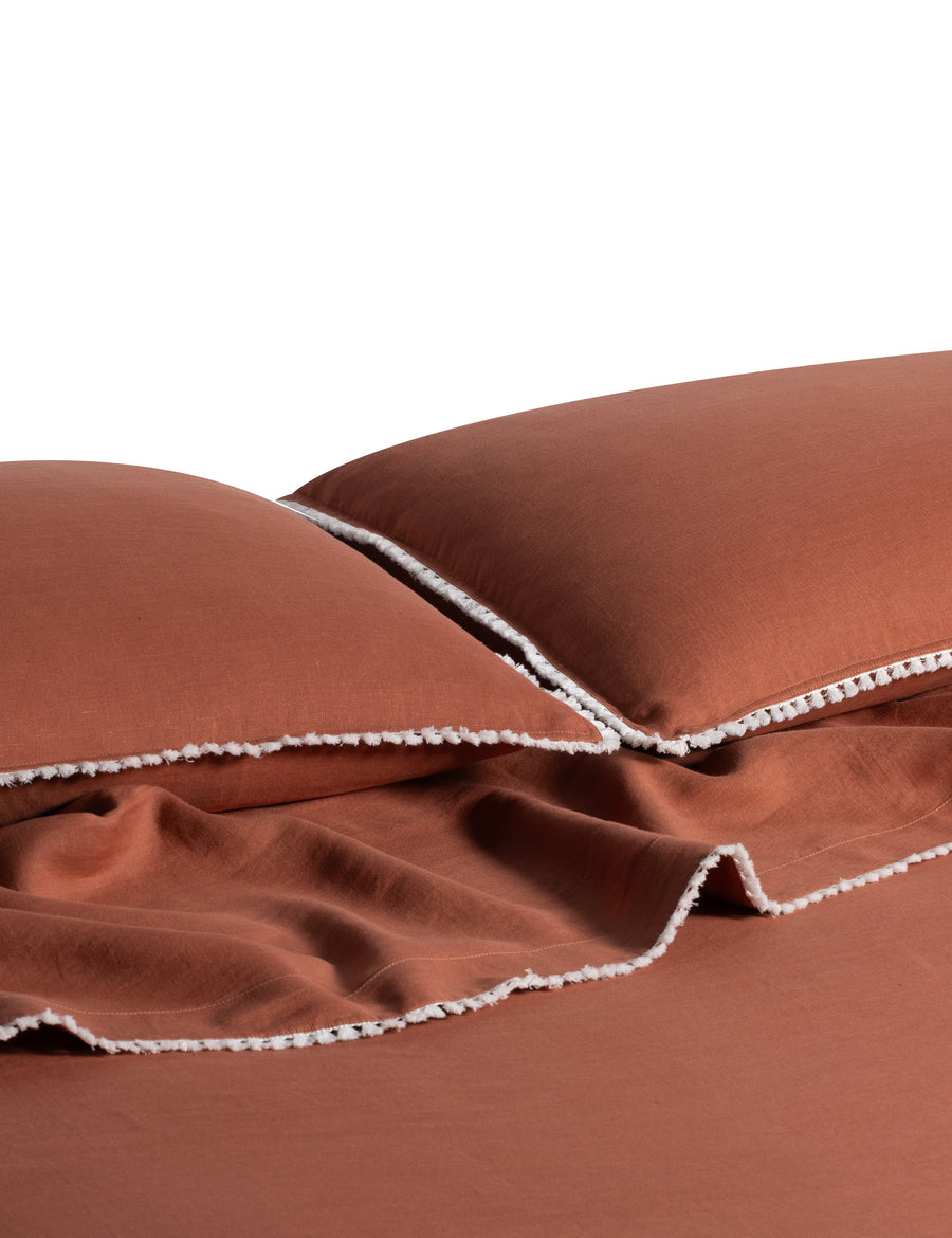 linen sheet set in rust colour and finished in our contrast organic cotton tassel trim