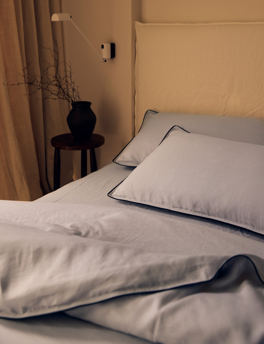 lifestyle shot of the linen piped sheet set in cement colour with charcoal piping with warm lighting