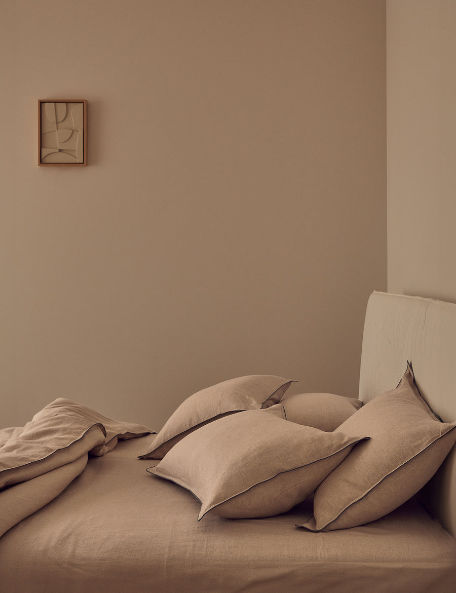 lifestyle shot of the linen piped sheet set in natural colour with liberty piping with rustic decor and warm ambience