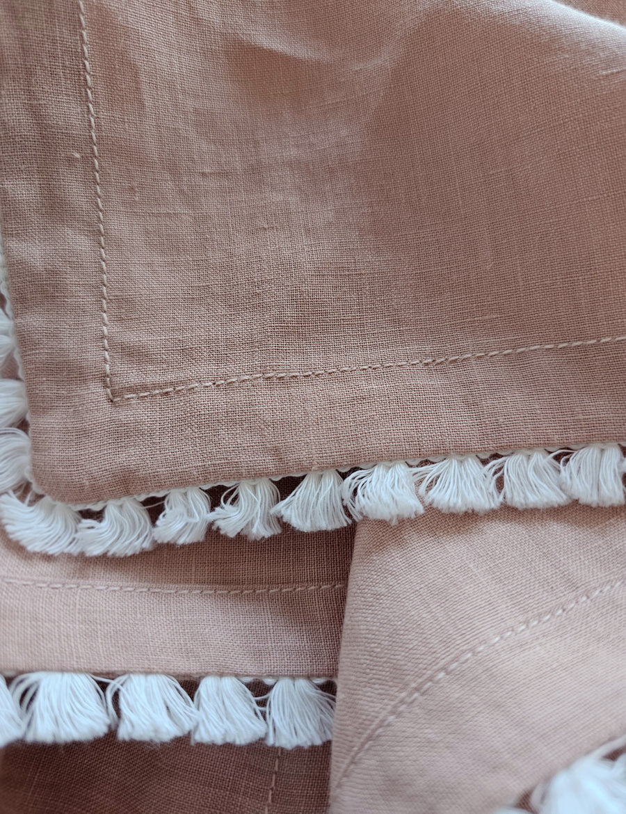 details shot of the linen table napkin in blush colour with cotton tassel trim in white