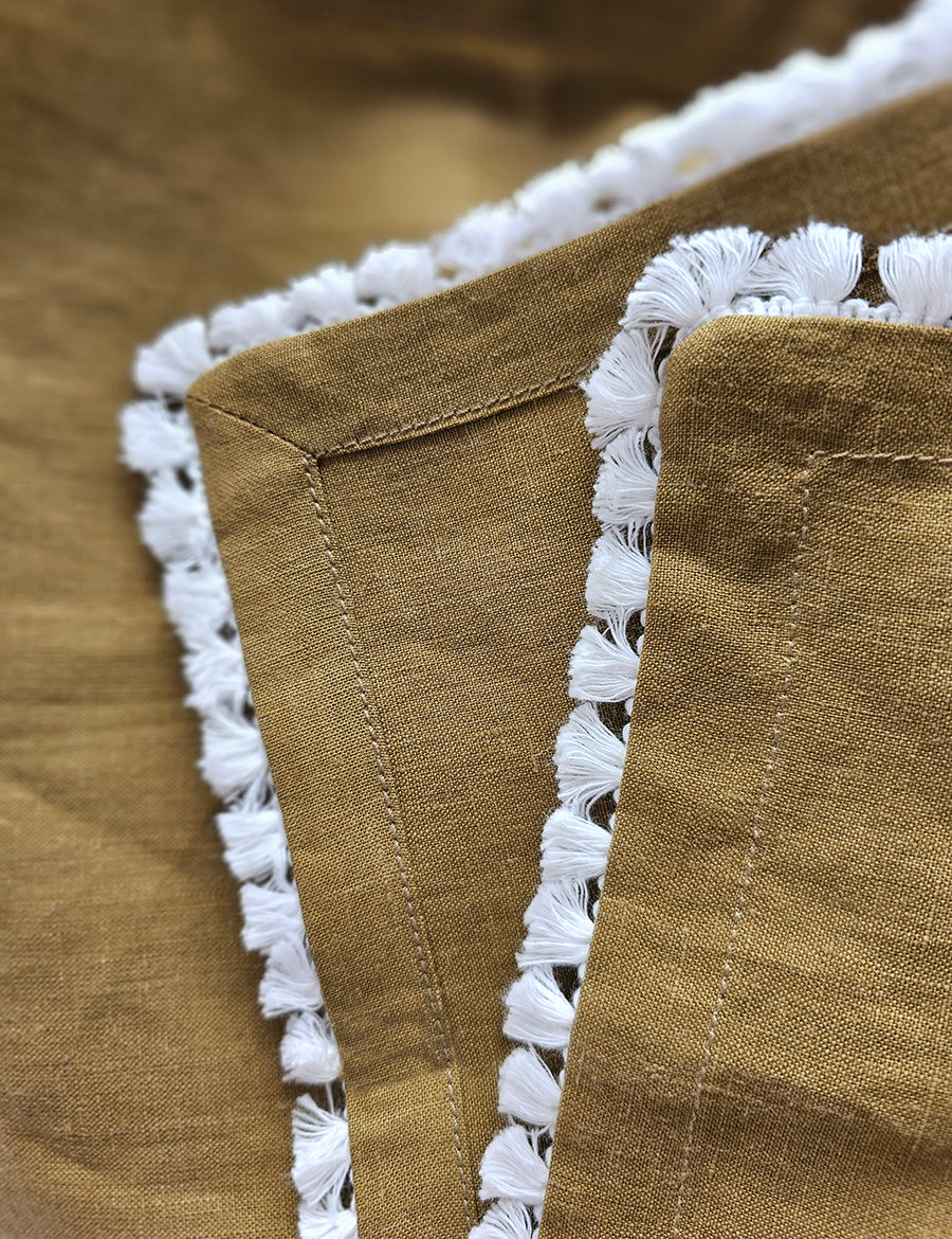 details shot of the linen table napkin in olive colour with cotton tassel trim in white