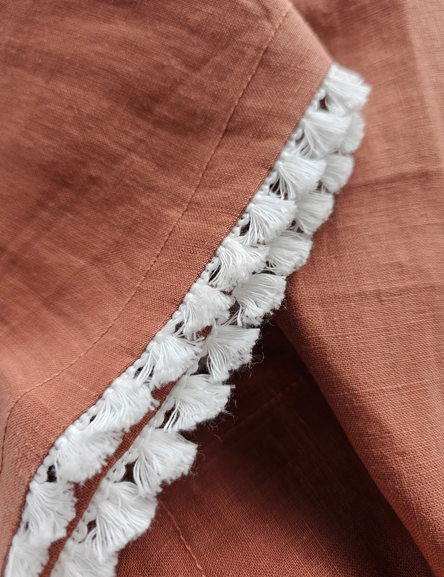 details shot of the linen table napkin in rust colour with cotton tassel trim in white