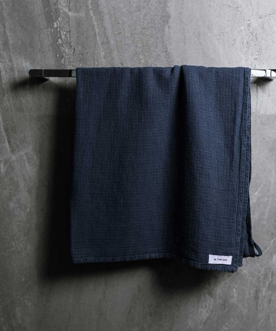 hanging linen jacquard bath towel in denim colour with dark grey marble wall