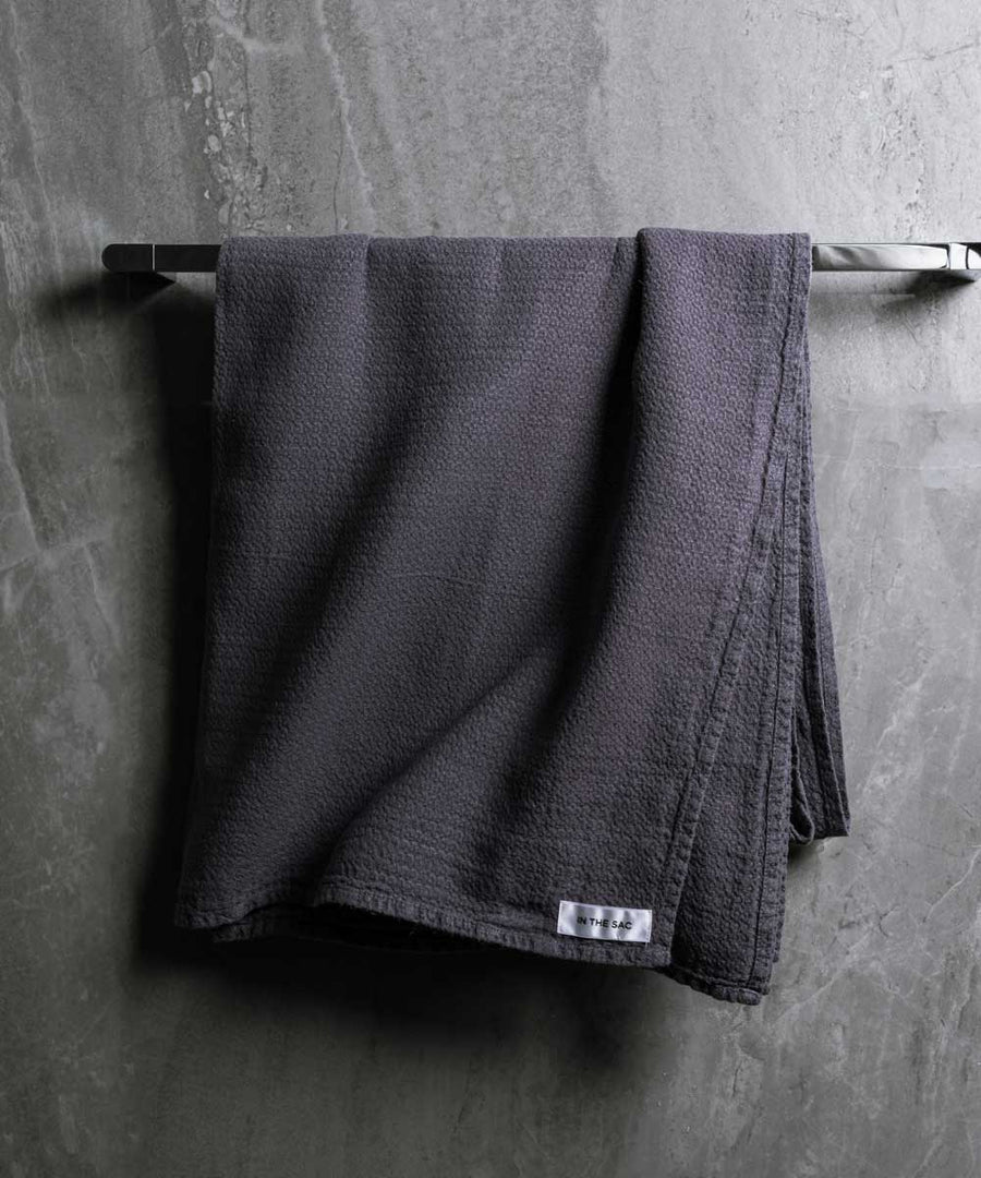 hanging linen jacquard bath towel in graphite colour with dark grey marble wall