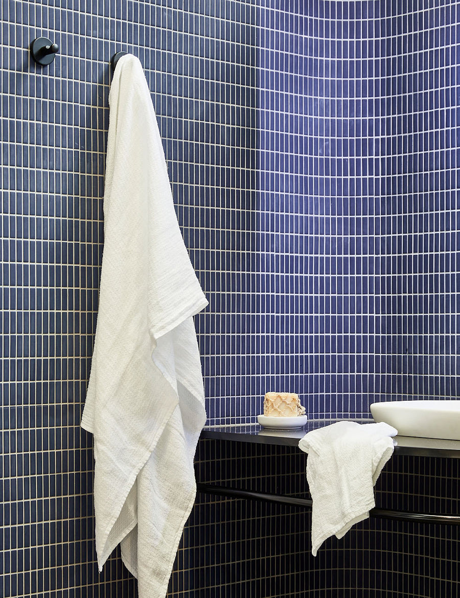 styled hanging pure linen jacquard bath towel in white colour with matching hand towel in a blue tiles bathroom