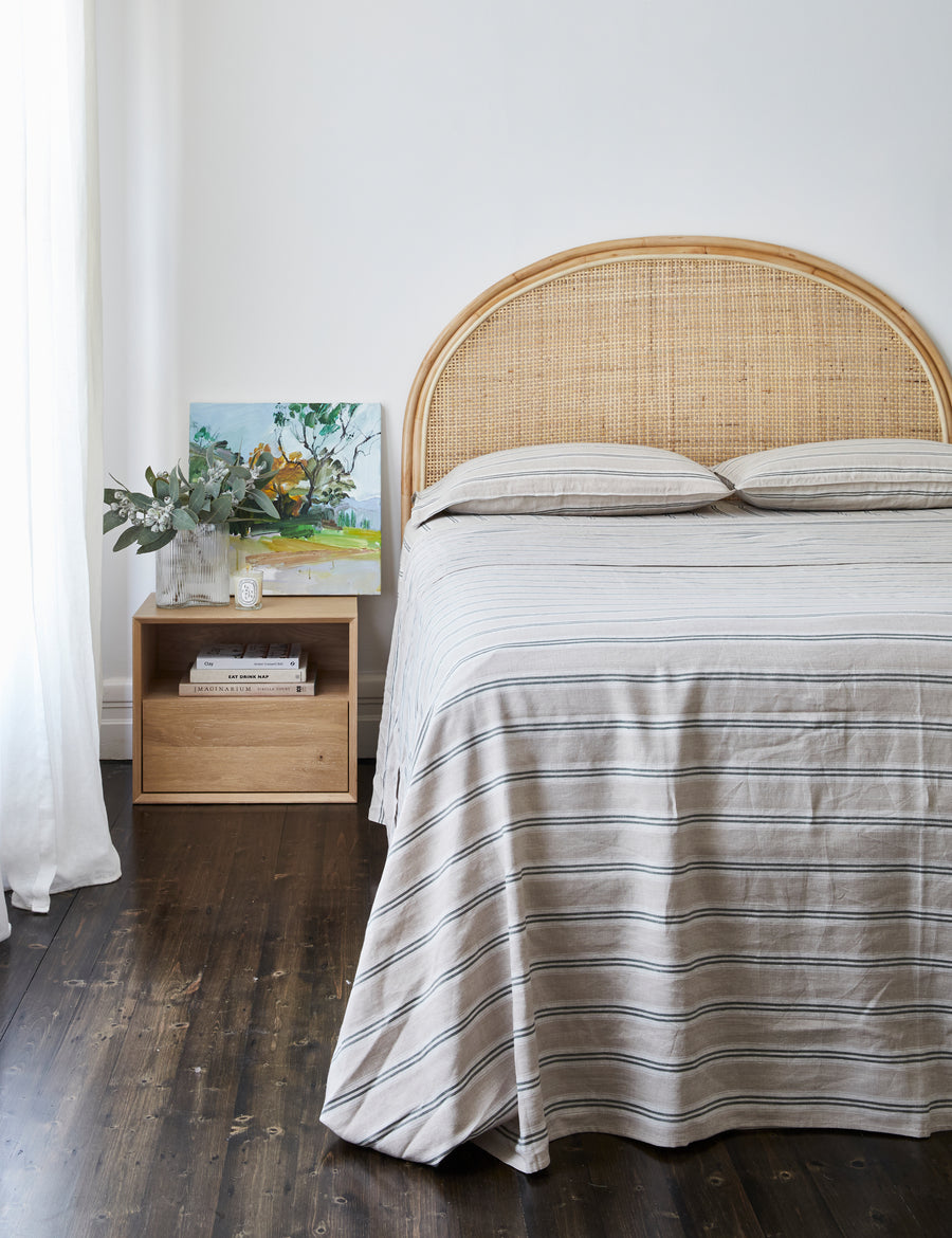 lifestyle shot of vintage stripe linen sheet set in cypress with beautiful painting with rattan headboard