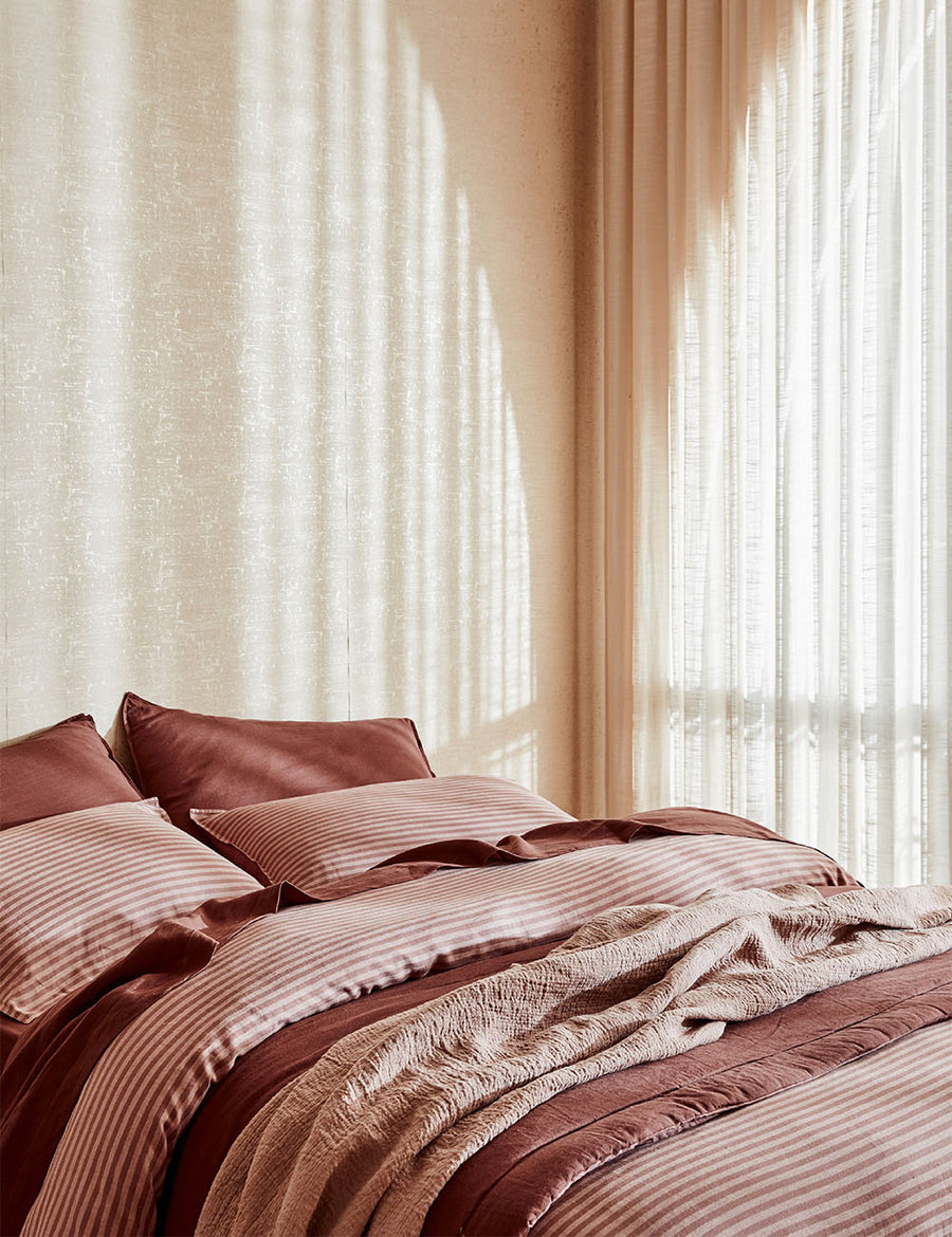 lifestyle shot of Chaplin Stripe Reversible Quilt Set in maple grenache paired with classic linen sheet set in grenache with vintage decor and arched window