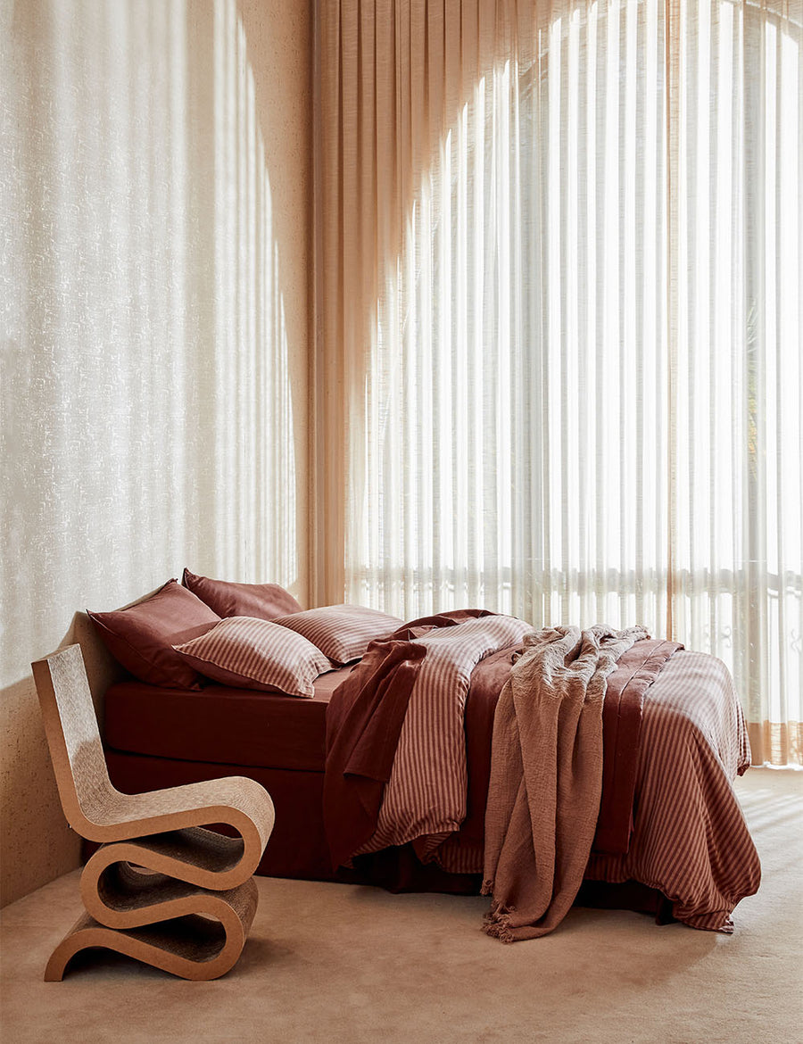 lifestyle shot of Chaplin Stripe Reversible Quilt Set in maple grenache paired with classic linen sheet set in grenache with vintage decor and arched window