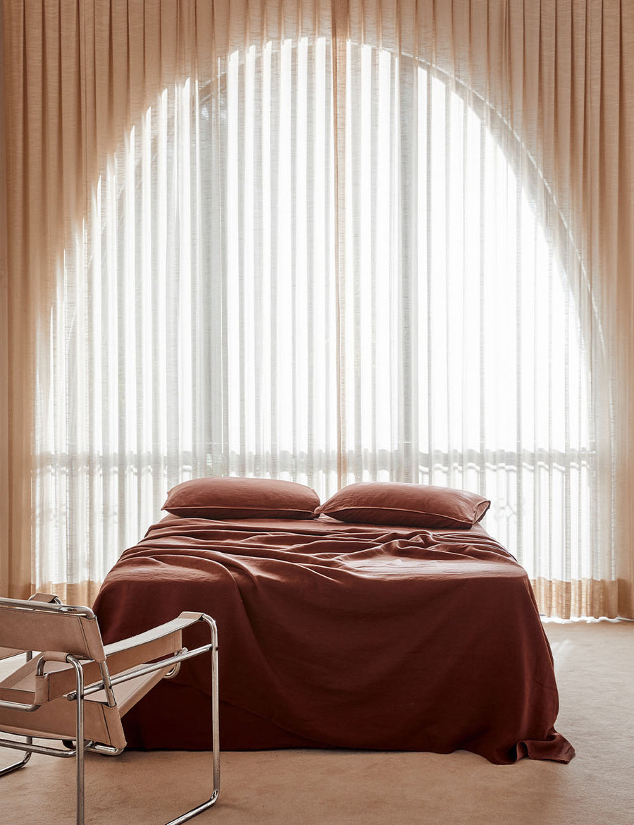 lifestyle shot of the classic linen sheet set in grenache colour with vintage decor and arched window