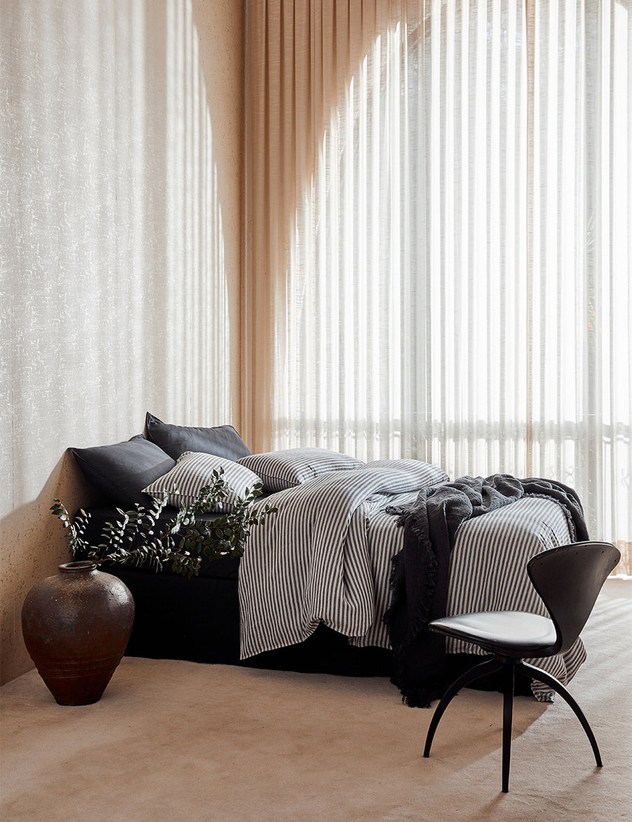 lifestyle shot of Chaplin Stripe Reversible Quilt Set in charcoal paired with classic linen sheet set in charcoal with vintage decor and arched window