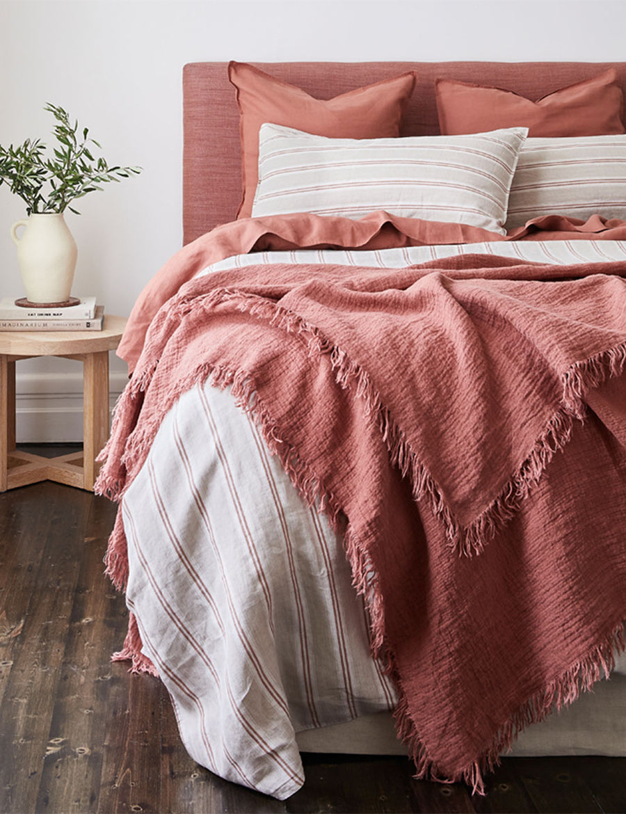 lifestyle shot of the textured linen throw in rust colour paired with stripes bedding and modern decor