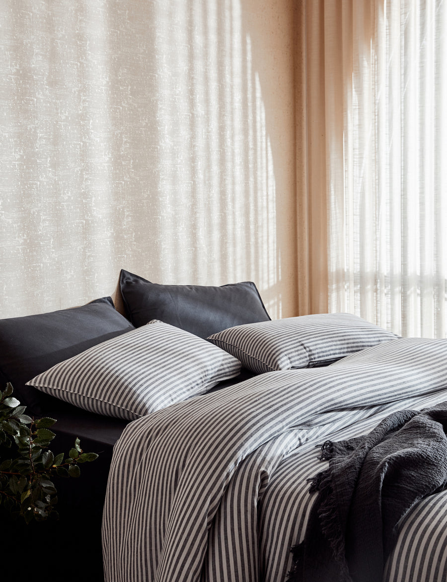 lifestyle shot of Chaplin Stripe Reversible Quilt Set in charcoal paired with classic linen sheet set in charcoal 