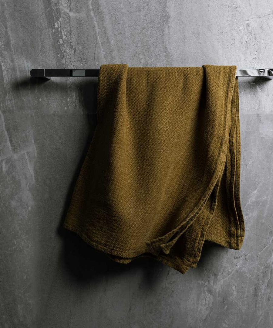 hanging photo of pure linen jacquard bath towel in olive colour with dark grey marble wall
