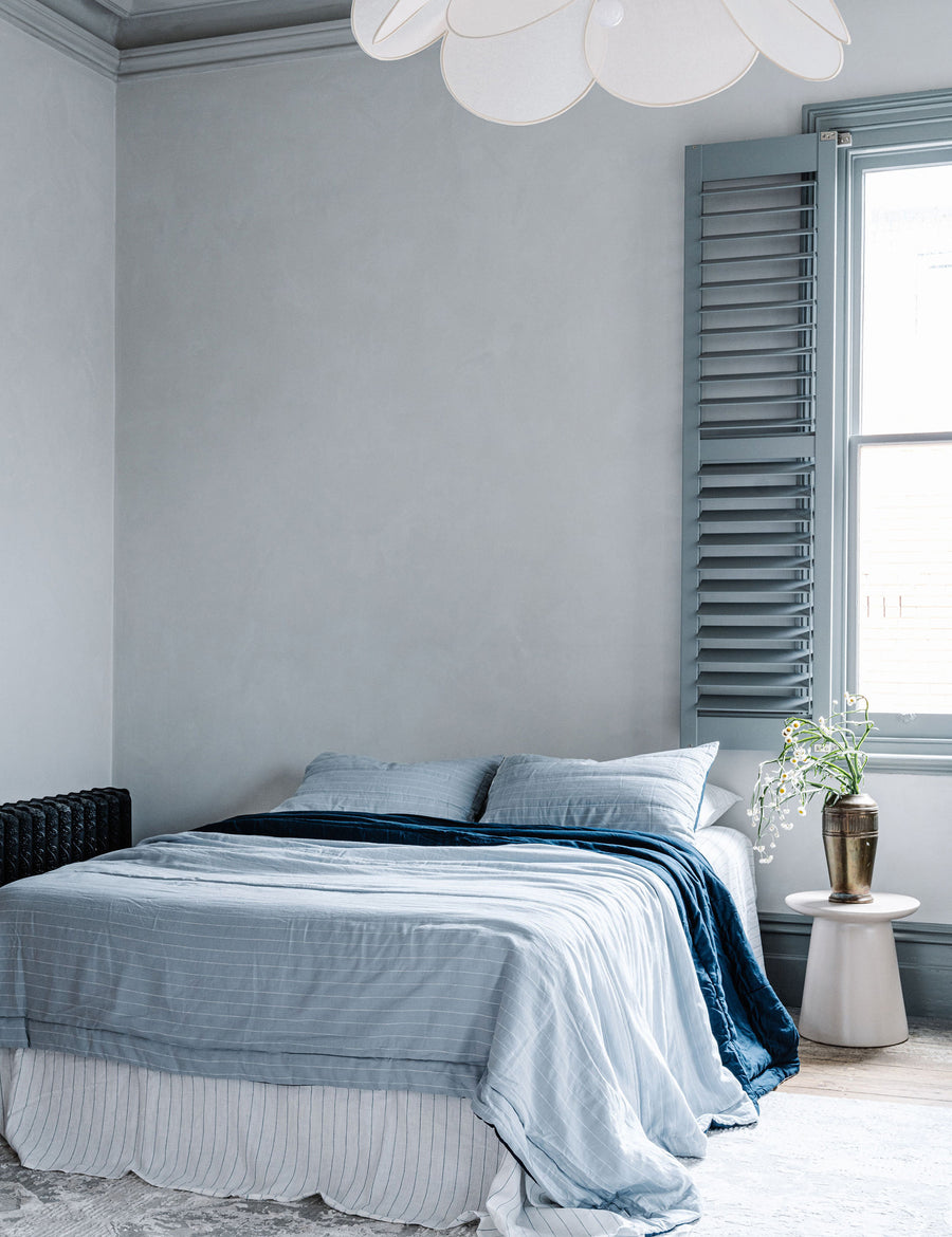lifestyle shot of the reversible linen quilted coverlet navy and cloud pinstripe paired with white cloud pinstripe sheet set with modern decor and blue window