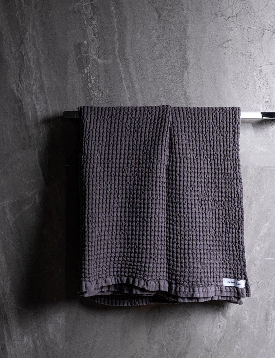 hanging photo of linen waffle bath towel in graphite colour with dark grey marble wall