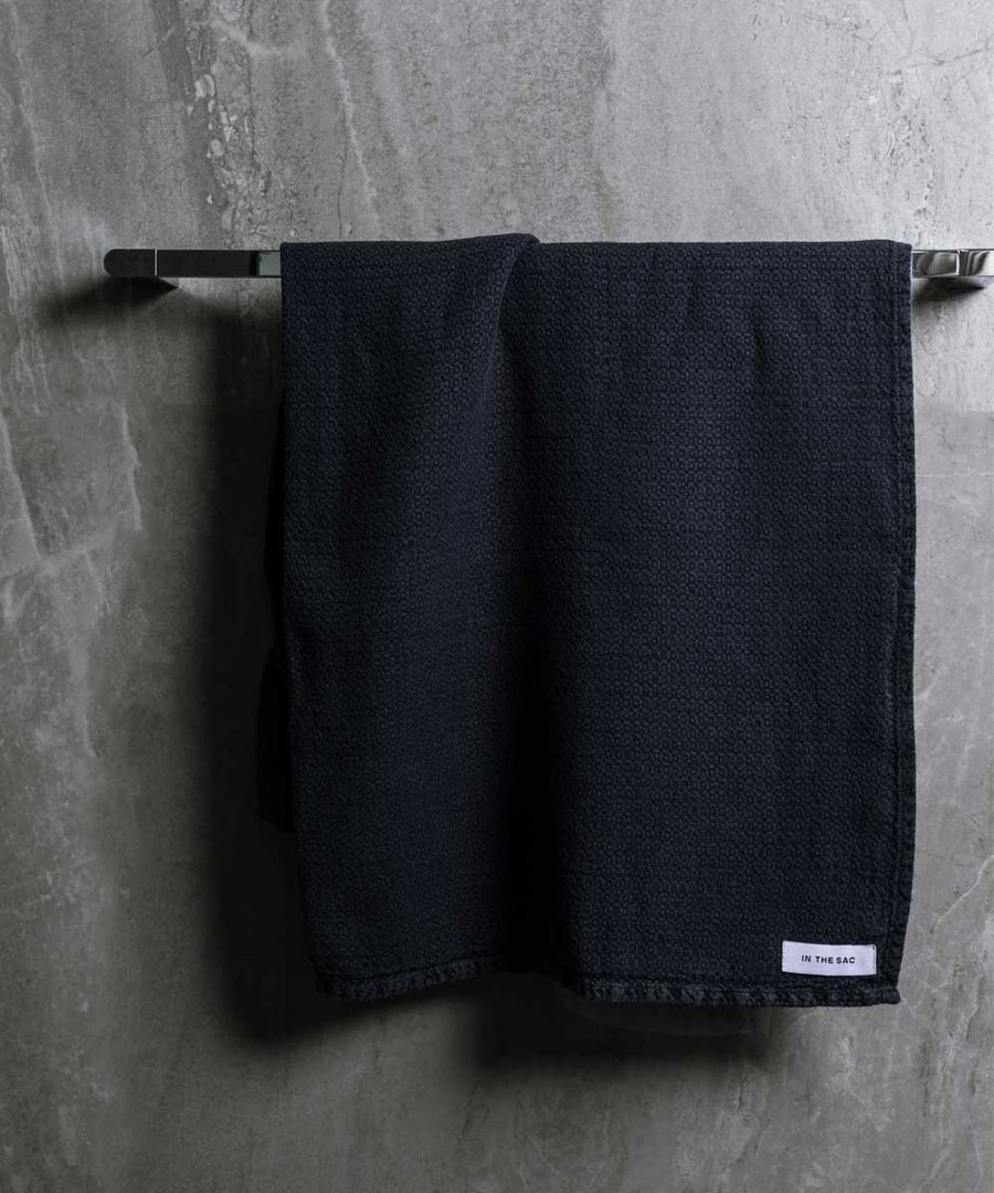 hanging linen jacquard bath towel in navy colour with dark grey marble wall