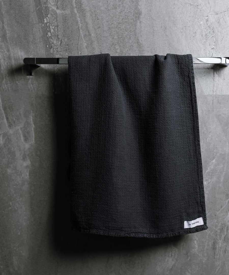 hanging linen jacquard bath towel in charcoal colour with dark grey marble wall
