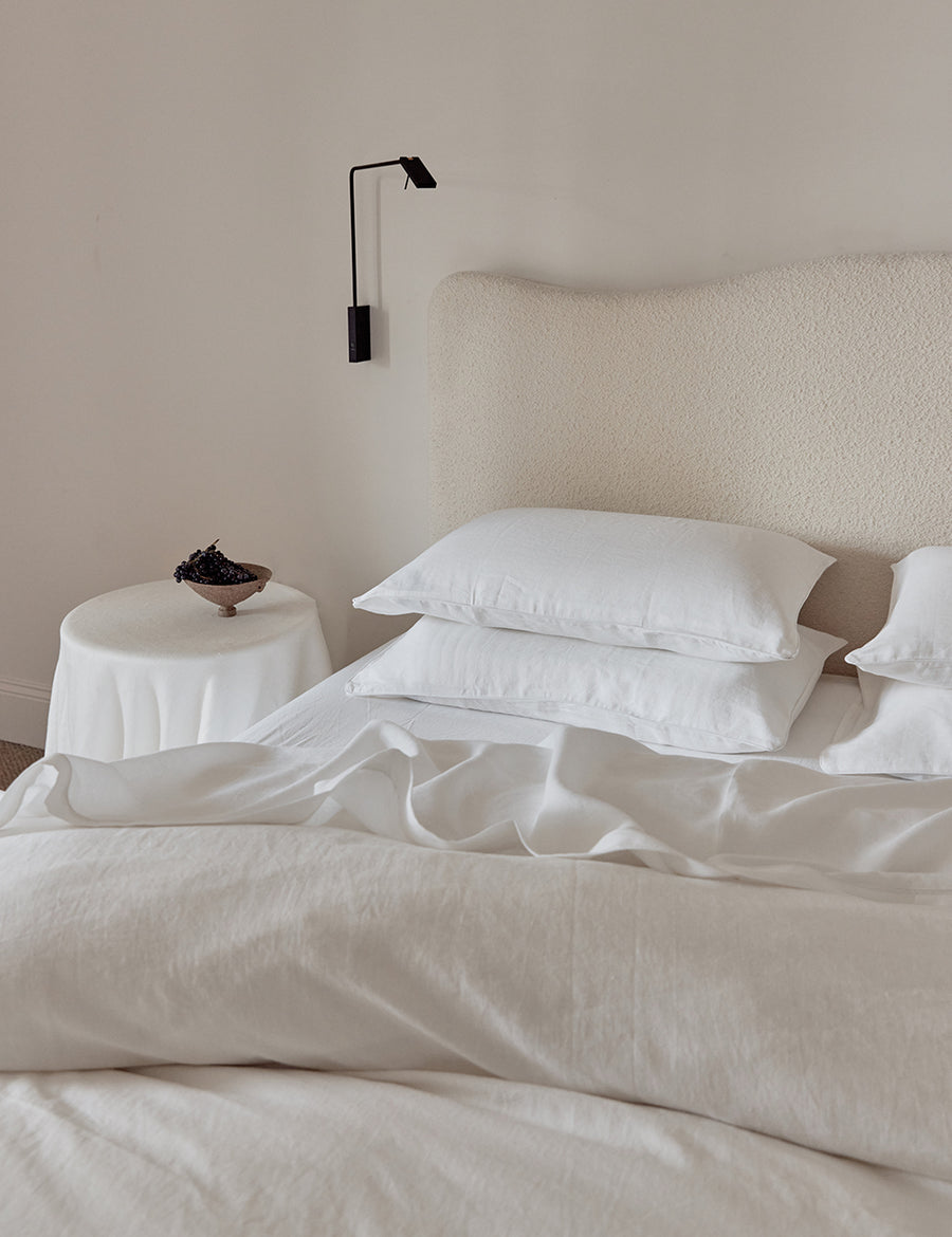 lifestyle shot of the linen piped quilt set in white colour with white piping with rustic decor and boucle headboard