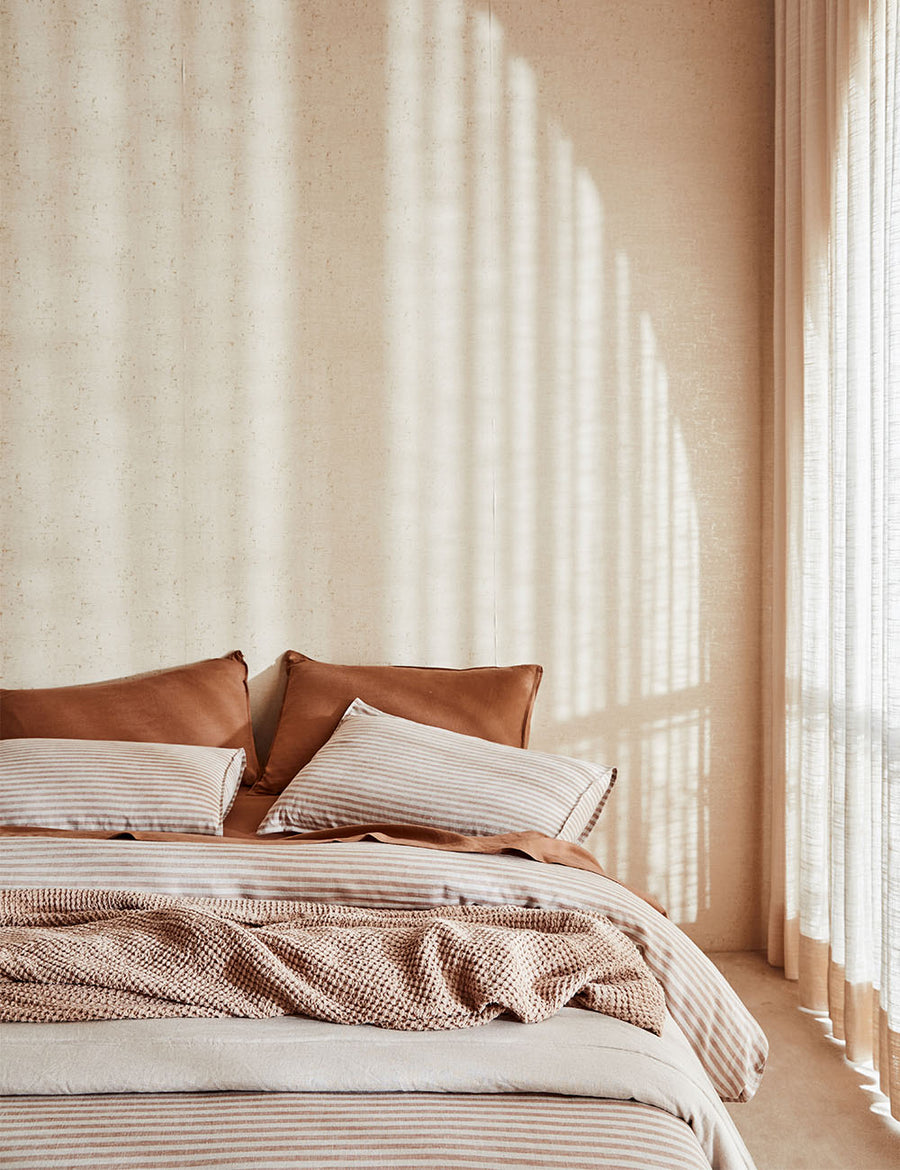 lifestyle shot of Chaplin Stripe Reversible Quilt Set in Caramel paired with classic linen sheet set in cognac with vintage decor and arched window