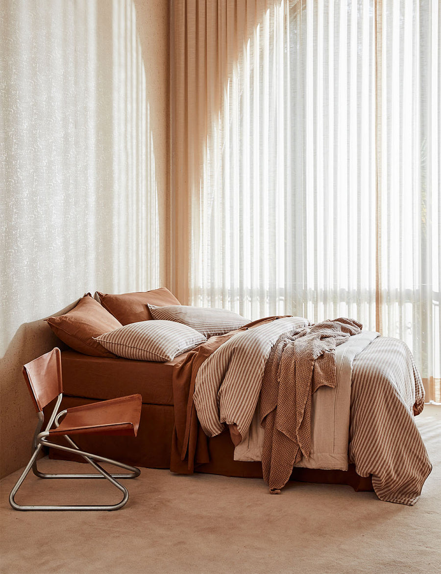 lifestyle shot of Chaplin Stripe Reversible Quilt Set in Caramel paired with classic linen sheet set in cognac with vintage decor and arched window