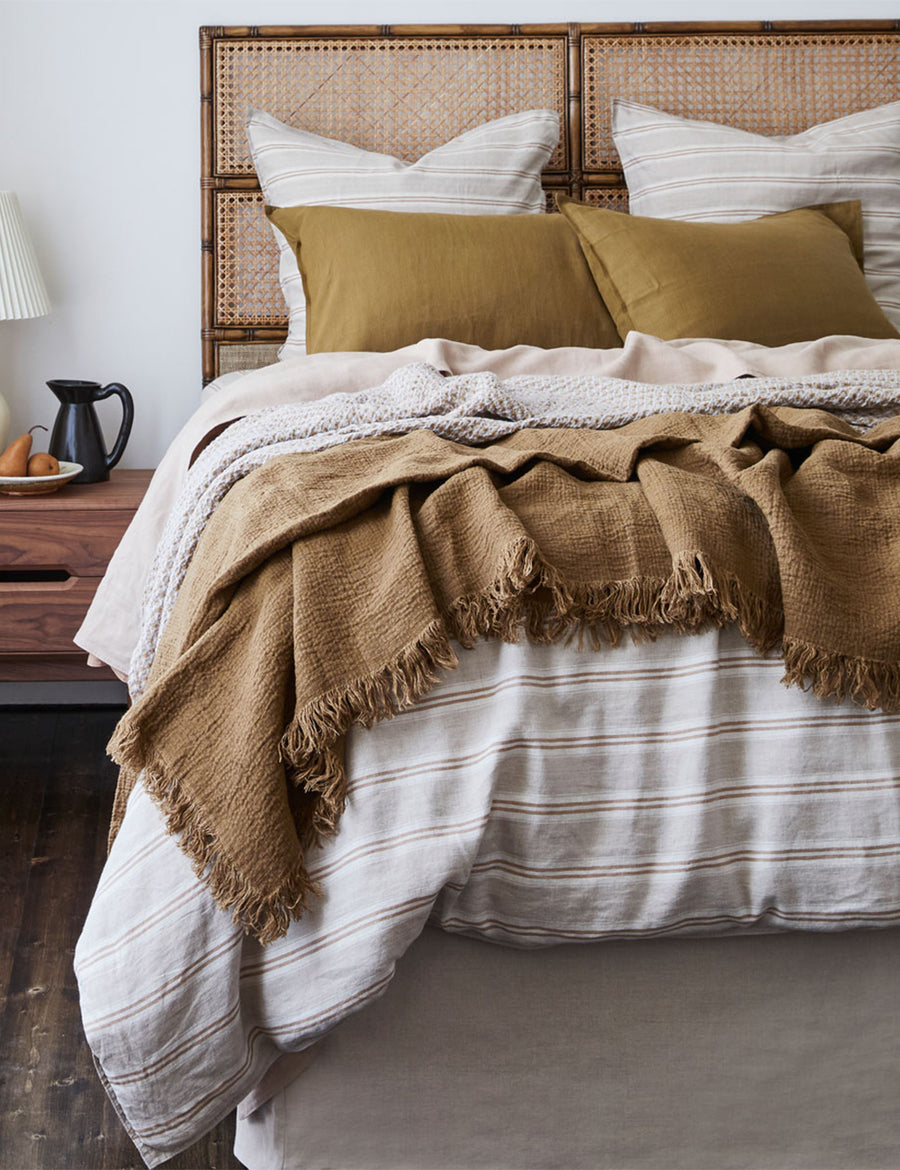 lifestyle shot of the textured linen throw in tobacco colour paired with stripes bedding and rattan headboard