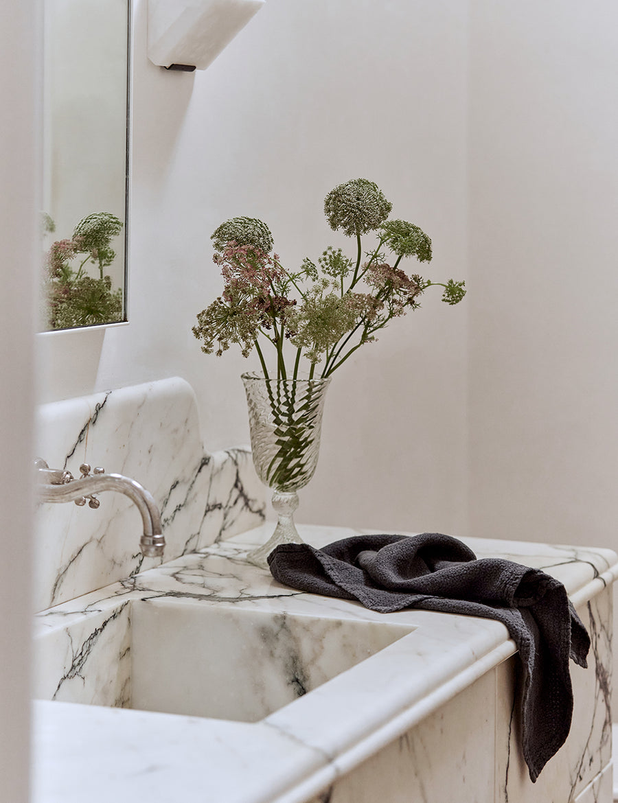 lifestyle shot of pure linen jacquard hand towel in charcoal colour with marble sink and decorative plants