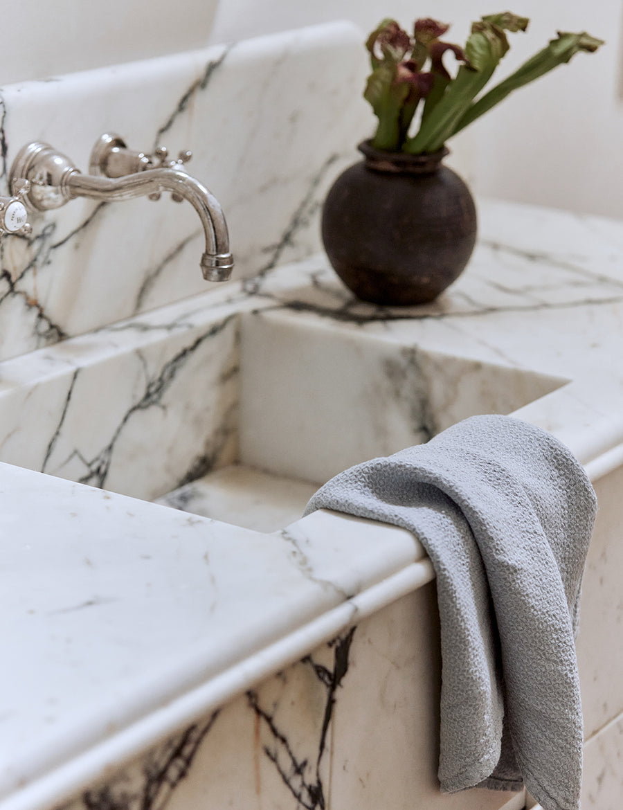 lifestyle shot of pure linen jacquard hand towel in cloud colour with marble sink and decorative plants