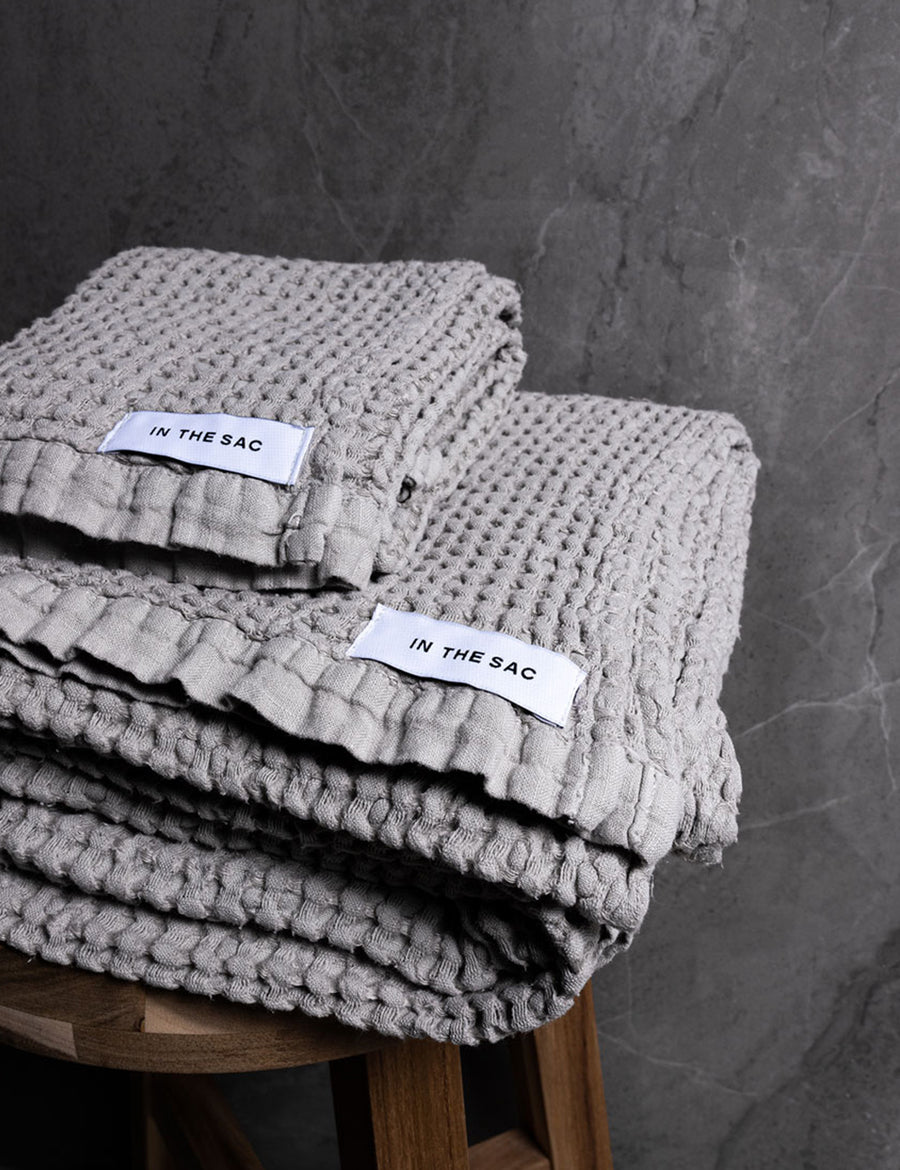 stacked photo of linen waffle hand towel in grey colour with matching bath towel on wooden stool