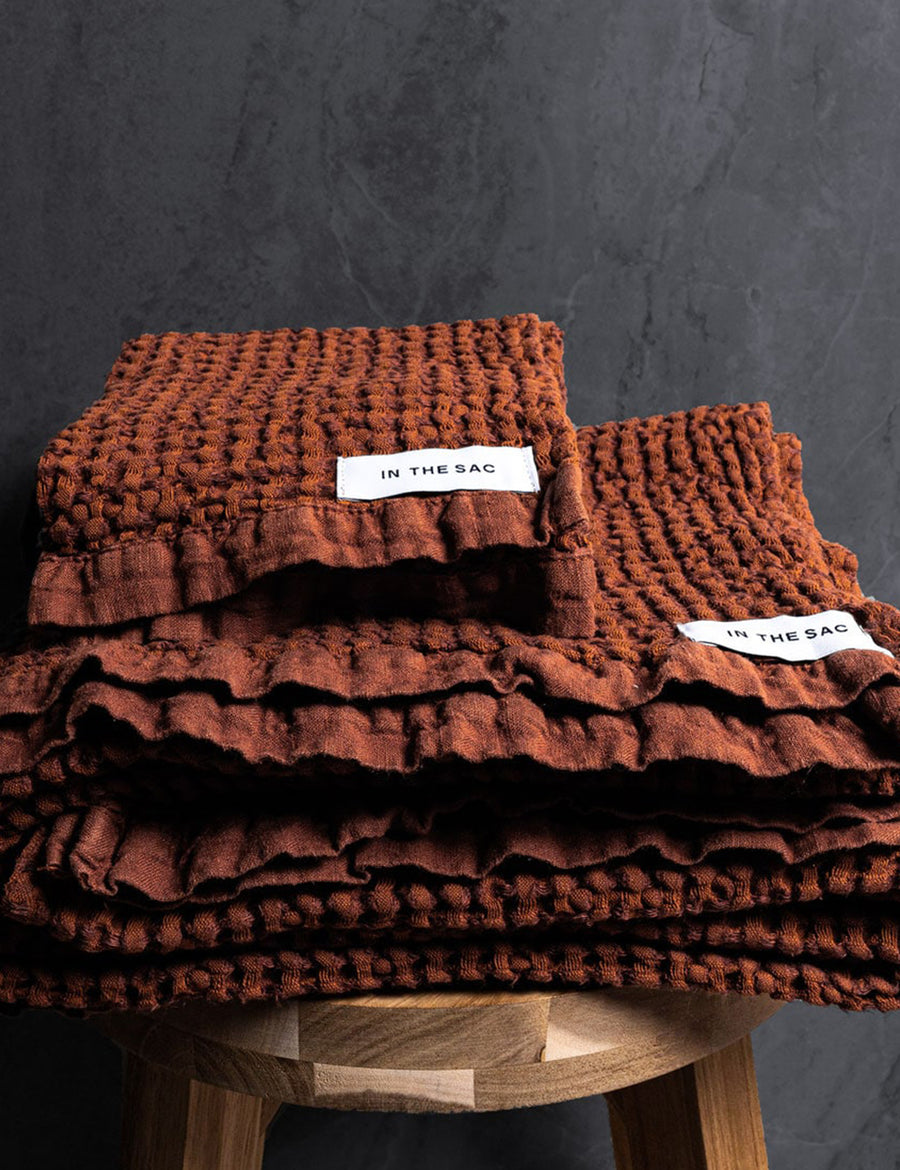 stacked photo of linen waffle hand towel in rust colour with matching bath towel on wooden stool
