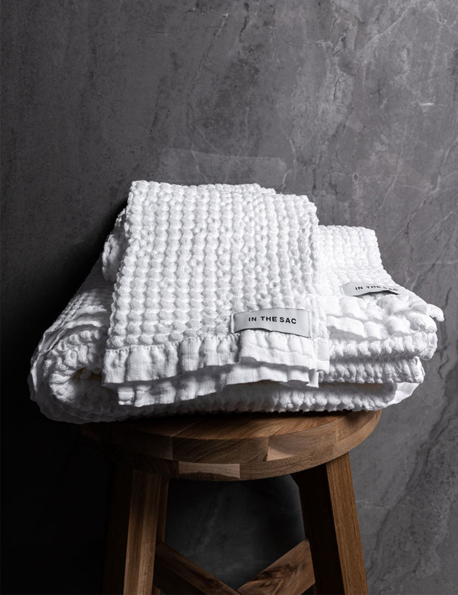 stacked photo of linen waffle hand towel in white colour with matching bath towel on wooden stool